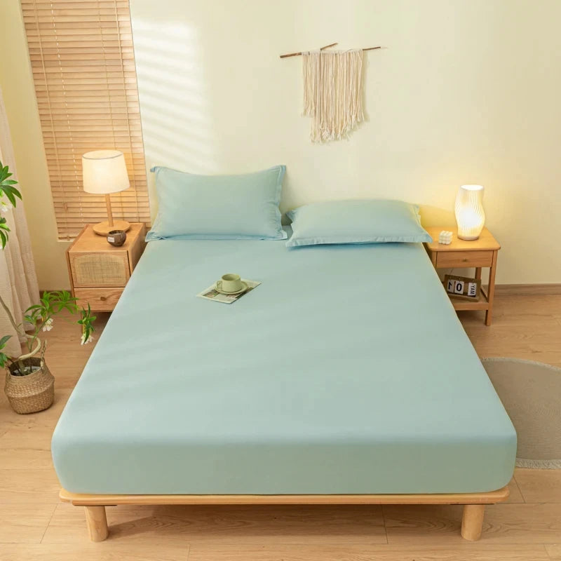 A light blue fitted sheet set with matching pillowcases is laid out on a wooden bed frame in a bright room.