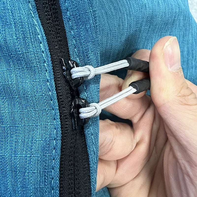 A hand is shown pulling apart a black zipper pull replacement clip with white string on a blue fabric.