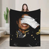 A woman holds up a black graphic plush throw blanket featuring a close-up portrait of a smiling face with sparkling details.