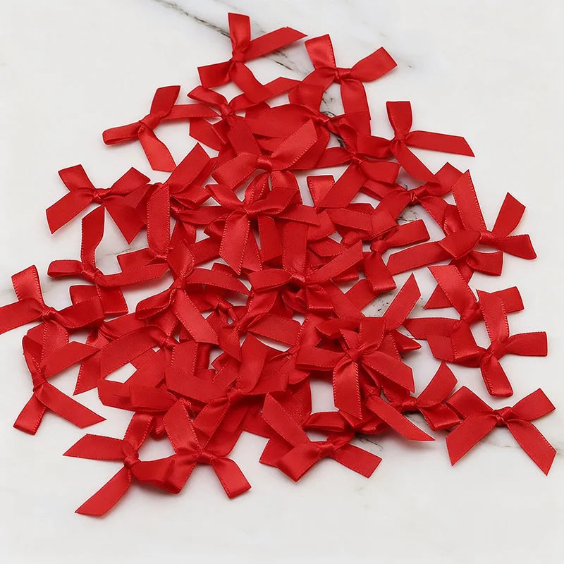A pile of small red satin ribbon bows scattered on a white marble surface.
