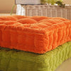 An orange tufted corduroy floor seat cushion stacked on a green one.