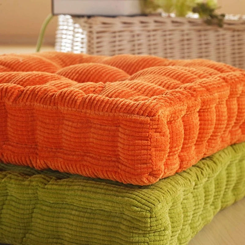 An orange tufted corduroy floor seat cushion stacked on a green one.
