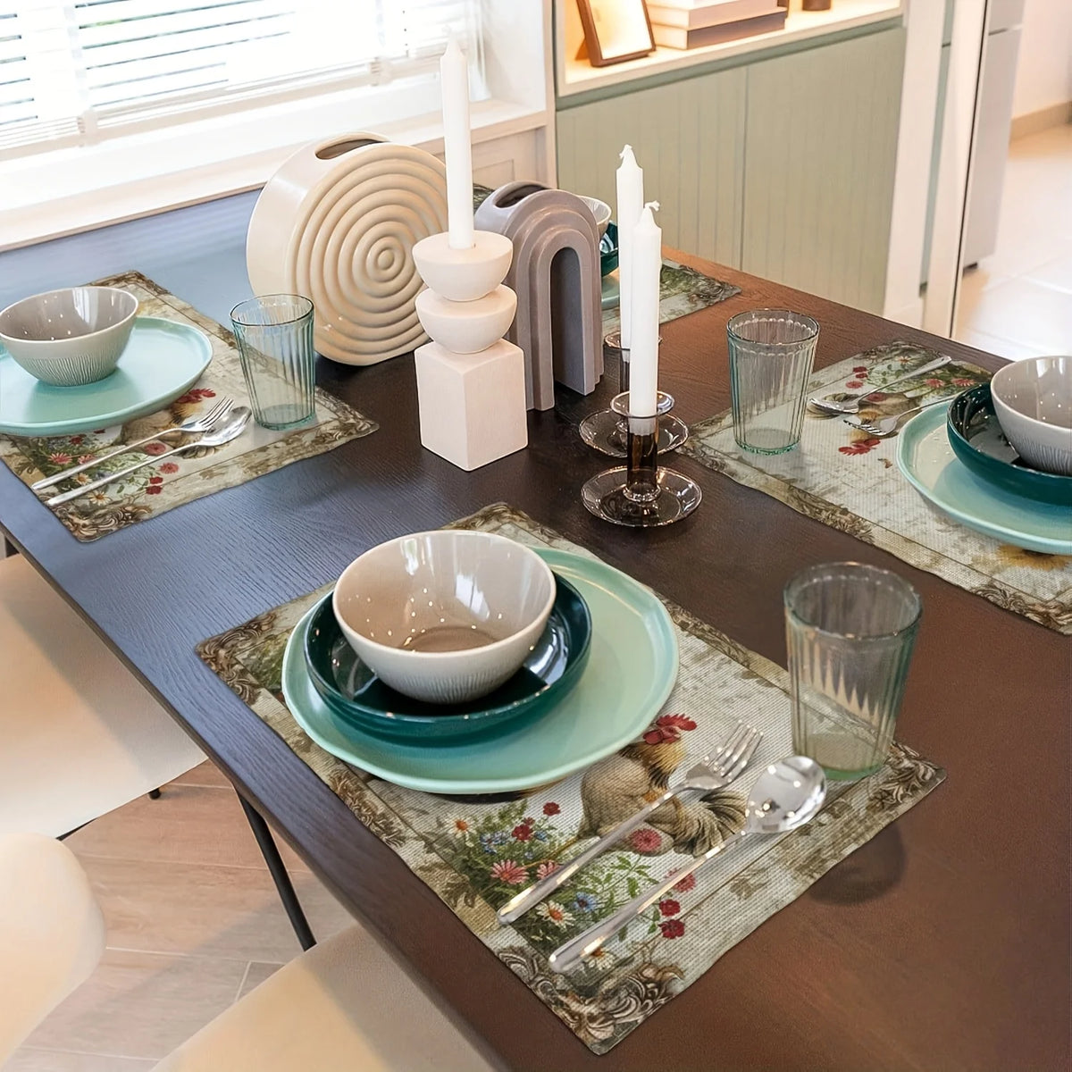 A dark wooden dining table set with vintage farmhouse rooster placemats, ceramic bowls, and glassware.