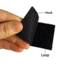 A hand holds a black embroidered patch set featuring a hook and a loop.