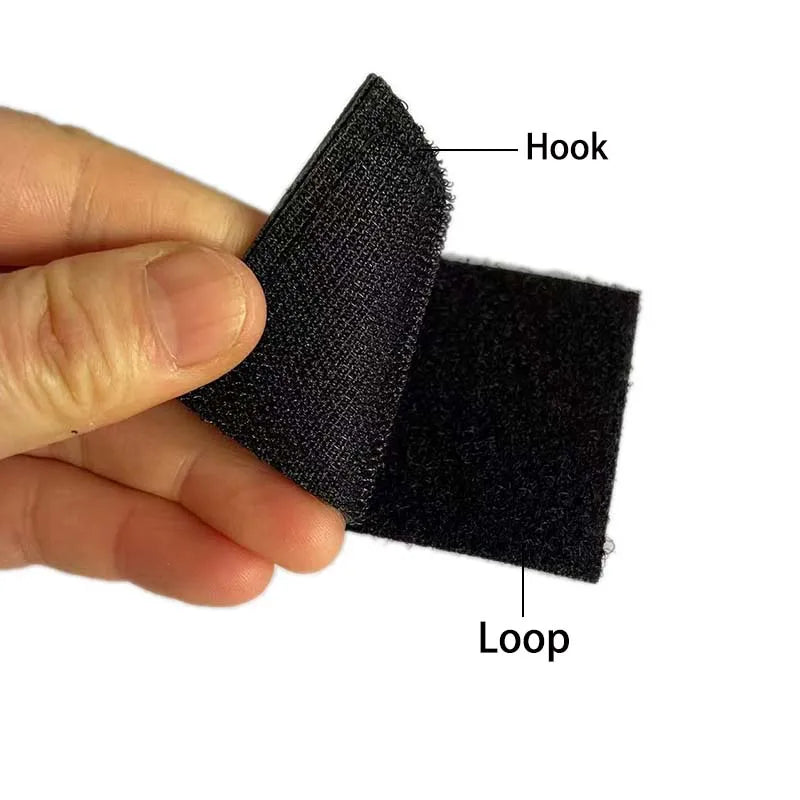 A hand holds a black embroidered patch set featuring a hook and a loop.