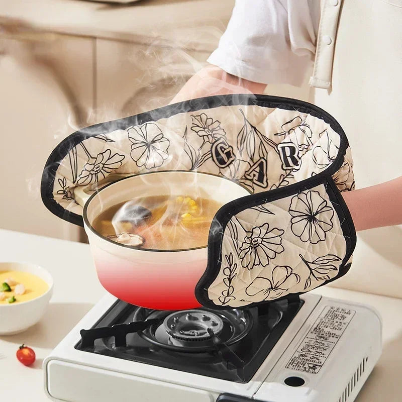 A person is using floral heat-resistant oven mitts to handle a pan on an electric stovetop.