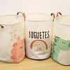 Three white fabric storage baskets with cartoon prints of a dinosaur, rainbow, and stars.