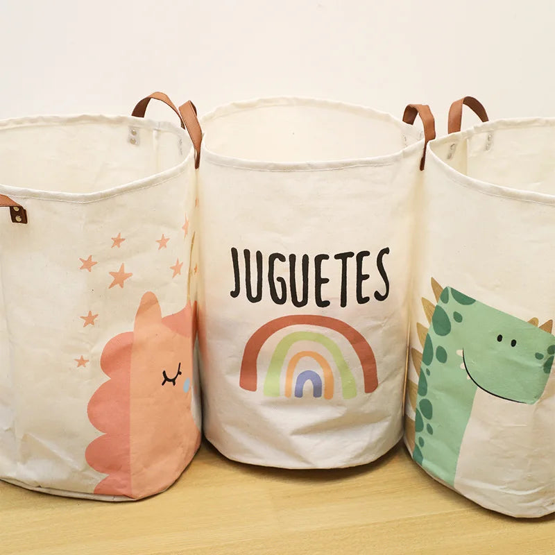 Three white fabric storage baskets with cartoon prints of a dinosaur, rainbow, and stars.