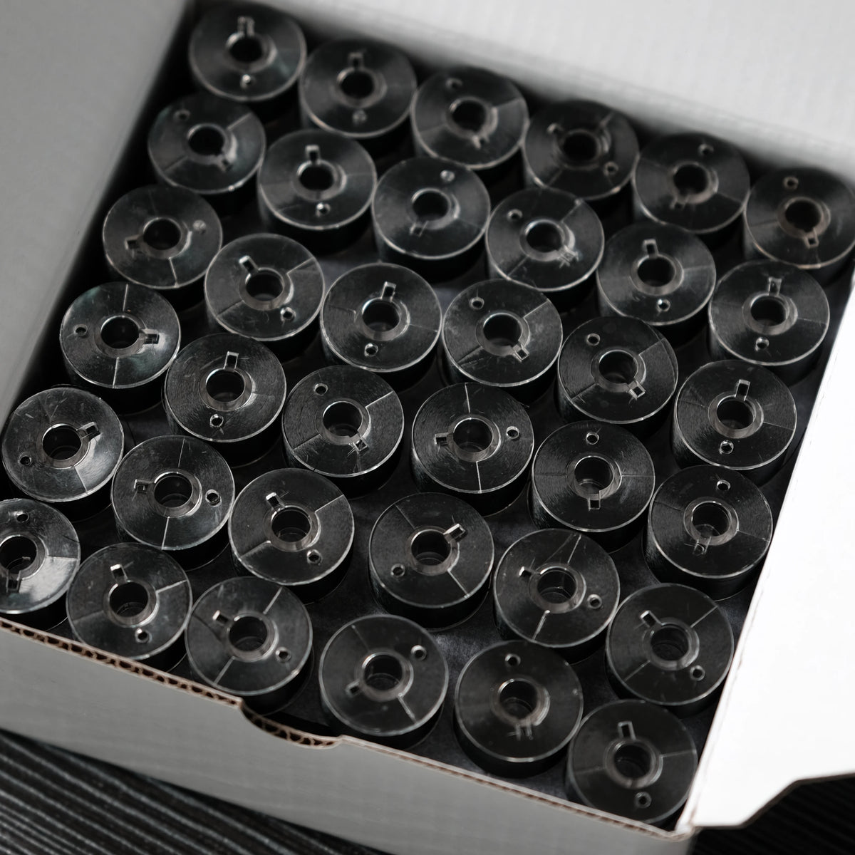 A grid of 144 black polyester embroidery bobbin threads packaged in a box.