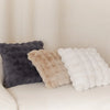 Three plush cushion covers in shades of gray, beige, and white resting on a light-colored sofa.