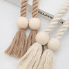 A pair of hand-woven wooden curtain tiebacks featuring natural beige fibers and round wooden beads.