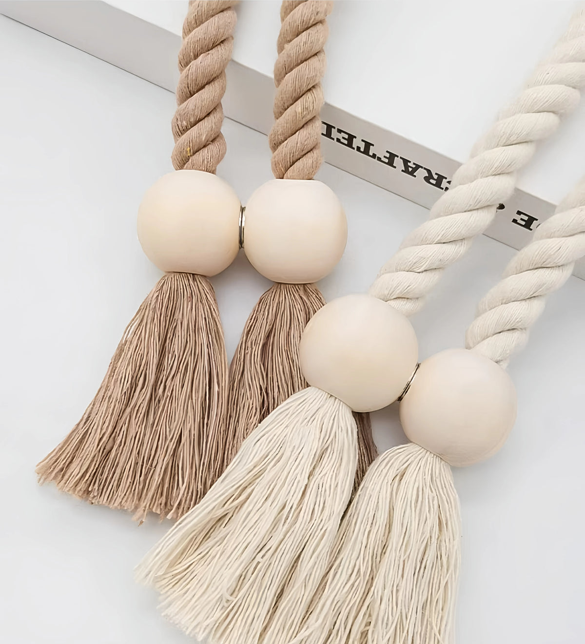 A pair of hand-woven wooden curtain tiebacks featuring natural beige fibers and round wooden beads.
