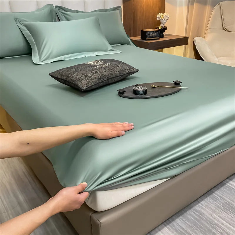 A luxury fitted bed sheet in sage green fabric is being placed onto a bed, with decorative pillows and accessories visible.