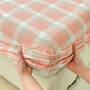 A close-up of a pink and white plaid fitted sheet being held by hands.