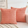 Two coral pink knitted textured throw pillow covers on a white sofa.