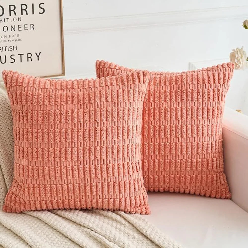 Two coral pink knitted textured throw pillow covers on a white sofa.