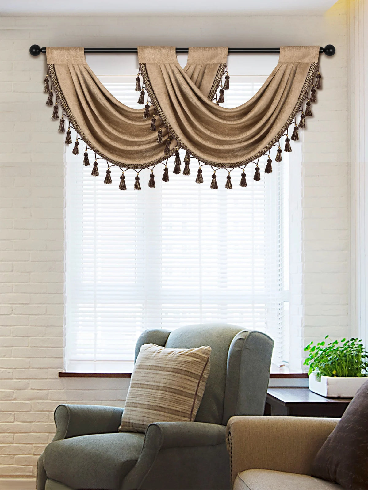 A beige window curtain valance with tassels hangs over a window in a bright room.