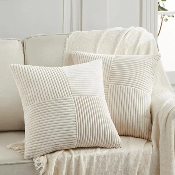 A close-up of a cream-colored patchwork pillow cover with vertical pleats on a light beige sofa.