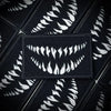A close-up of a black tactical hook and loop emblem patch with white stylized teeth design.