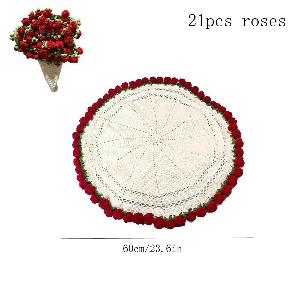 A round white knitted floral blanket with a red border and a small bouquet of red roses.