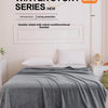 A gray velvet blanket is draped over a bed, set against a light wall with a framed sign promoting the Winter Story Series.