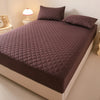 A dark purple quilted mattress protector with matching pillows on a bed.