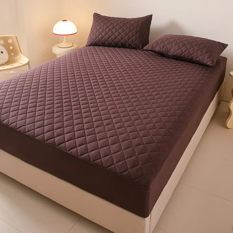 A dark purple quilted mattress protector with matching pillows on a bed.