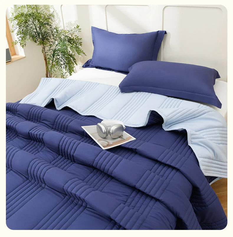 A navy blue quilted blanket and matching pillows are displayed on a bed with white linens.