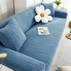 A light blue stretchable sofa cover with white floral cushions and a small plate on the seat.
