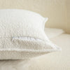A close-up of a white textured boucle throw pillow cover with a zipper detail on a light cream sofa.