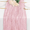 A pink cheesecloth table runner with a floral arrangement and gold-toned silverware.