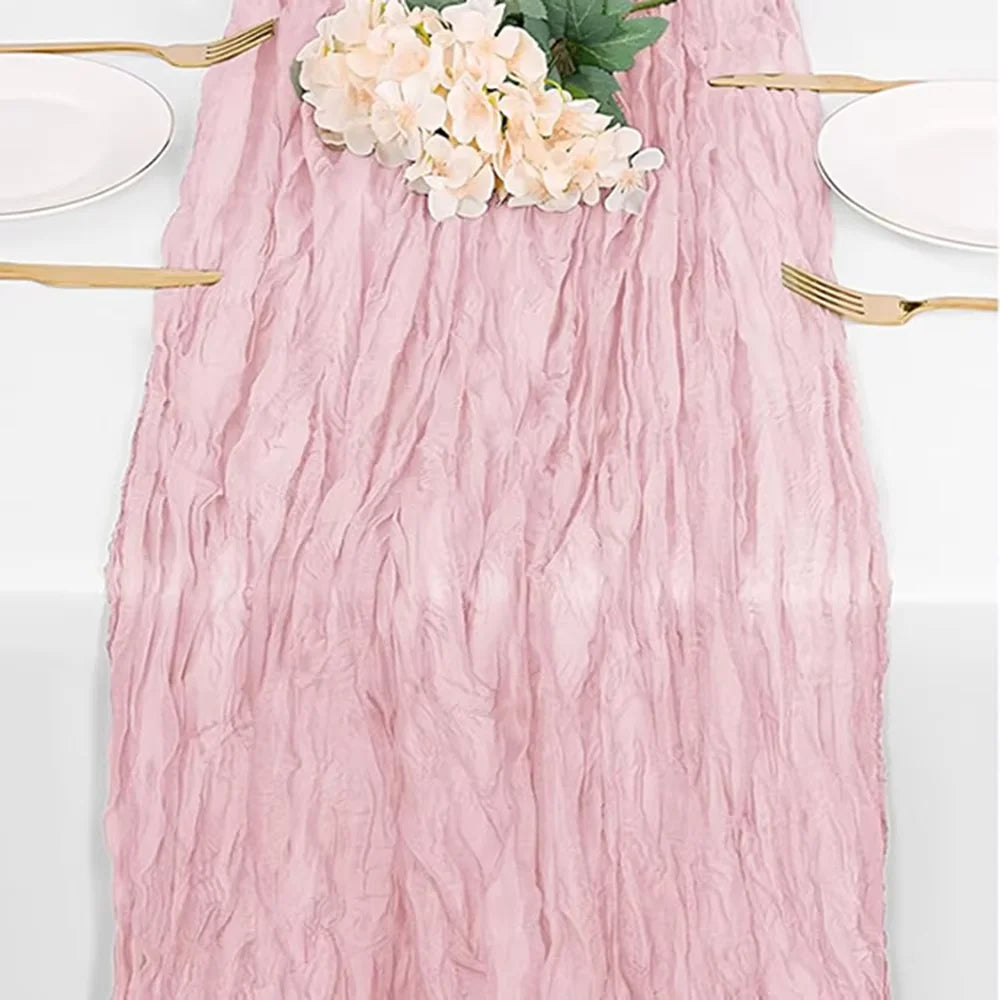 A pink cheesecloth table runner with a floral arrangement and gold-toned silverware.