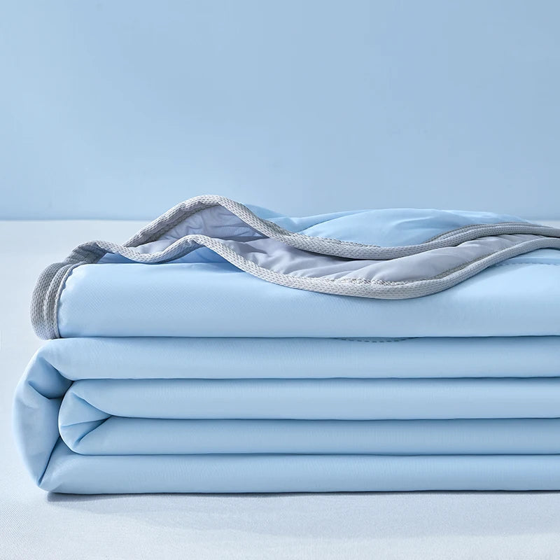 A stack of light blue cooling fiber blankets folded neatly on a white surface.