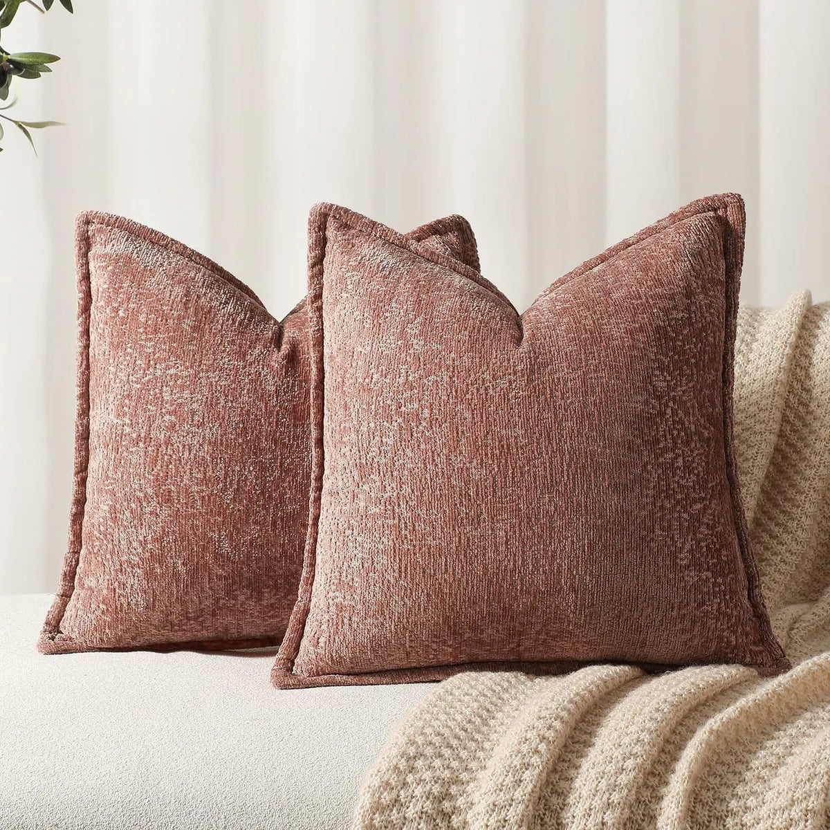 A close-up of a textured, dusty rose chenille throw pillow resting on a beige knitted blanket.