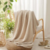 A beige ultra-soft 100% cotton gauze blanket draped over a wooden chair and resting on a woven seat.