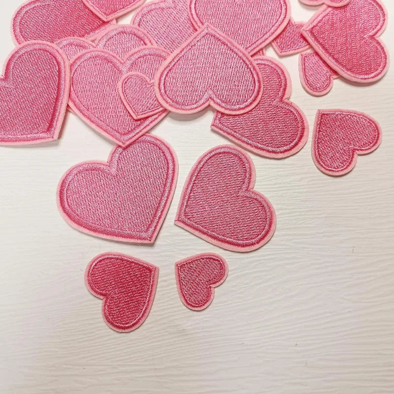 A collection of 24 pink iron-on love heart embroidered patches for DIY clothing.