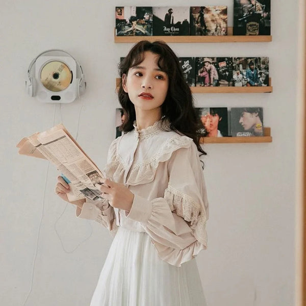 A young woman wearing a cream-colored retro lace long sleeve blouse and white skirt, holding a newspaper.