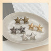 A collection of silver and gold metal star brooch pins arranged on a white plate next to a page of text.