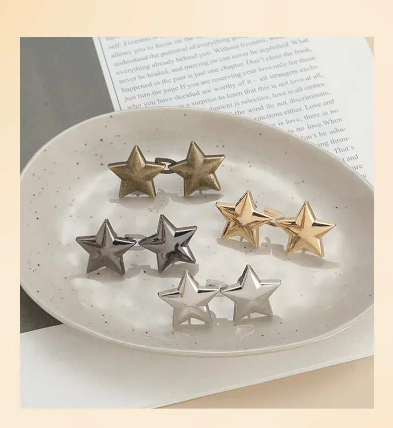 A collection of silver and gold metal star brooch pins arranged on a white plate next to a page of text.