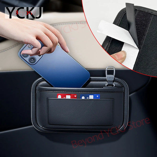 A hand places a smartphone into a black universal car organizer storage bag inside a car console.
