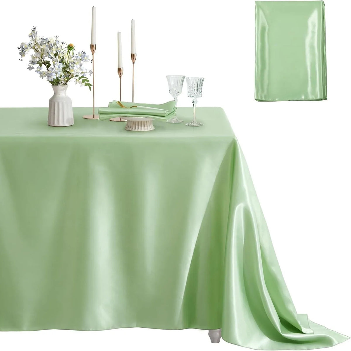 A light green satin tablecloth set for elegant dining featuring a centerpiece of white flowers and tall candles.