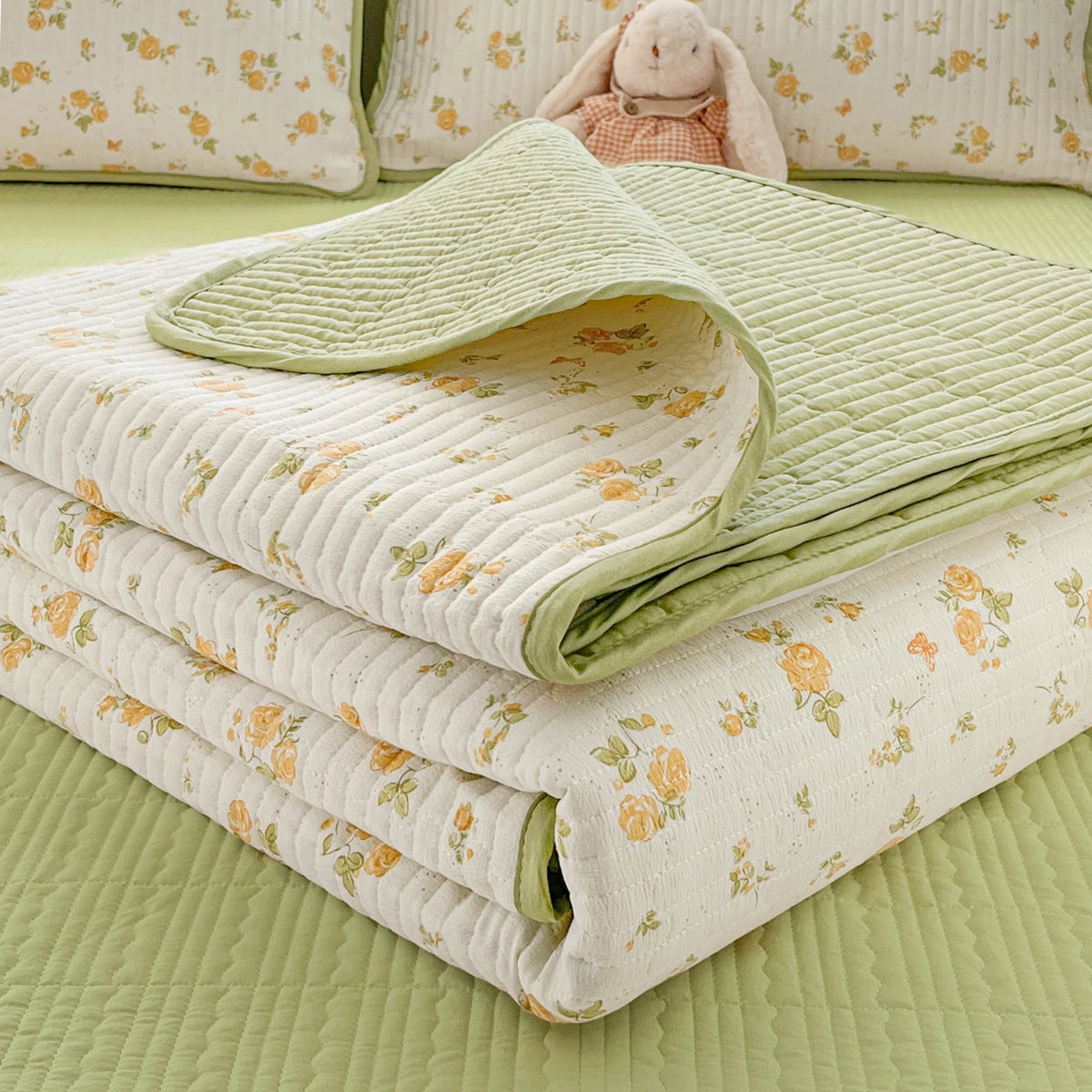 A stack of light green and cream quilted blankets with floral patterns resting on a lime green surface.