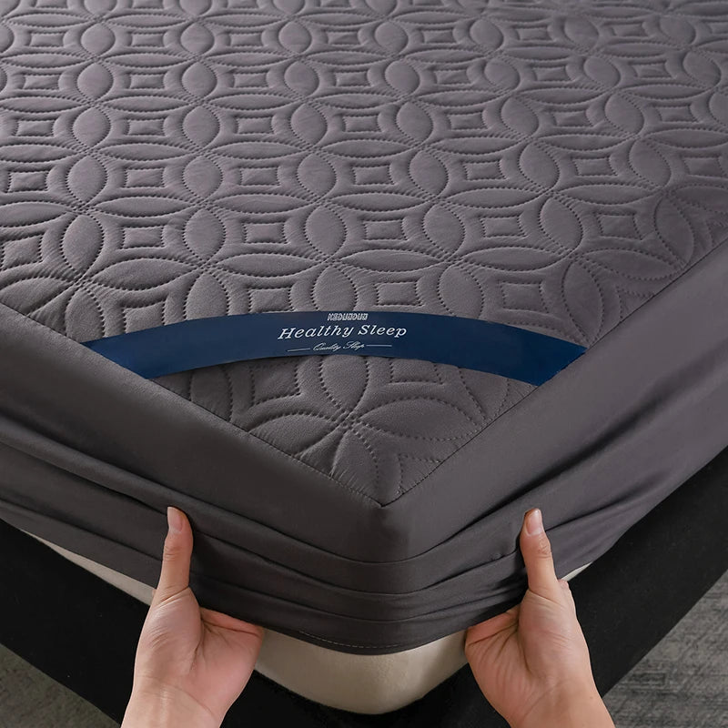 A hand is holding a gray quilted mattress protector with the Healthy Sleep branding.