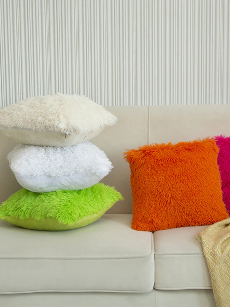 A set of two faux fur throw pillows in cream, white, and bright orange resting on a light-colored sofa.
