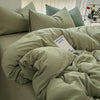 A bed with a light sage green duvet cover and pillows, featuring a white tag that reads GROOVY DAYS LD INEL.