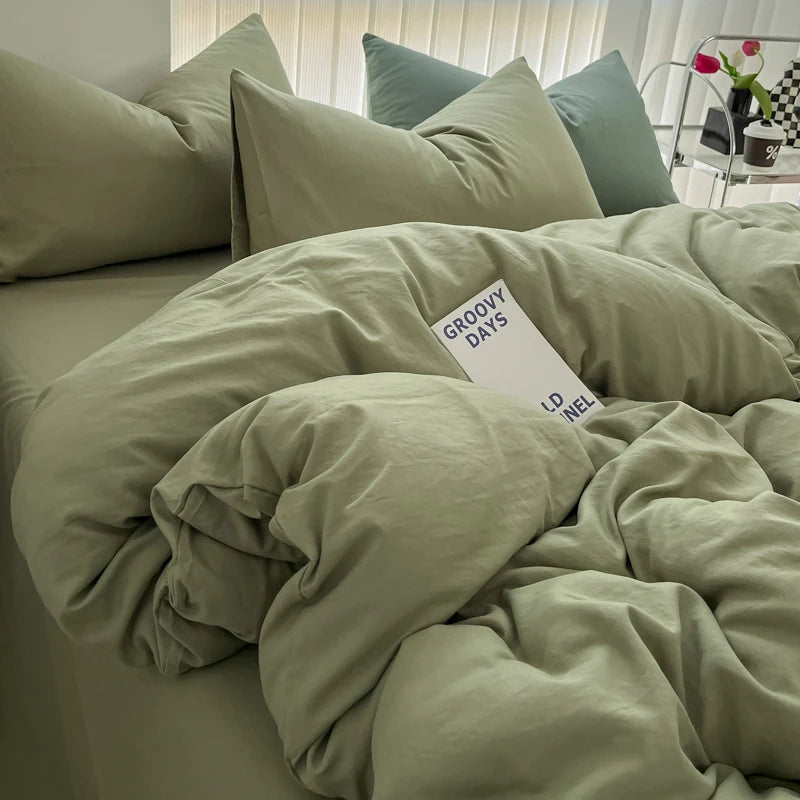 A bed with a light sage green duvet cover and pillows, featuring a white tag that reads GROOVY DAYS LD INEL.