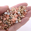 A hand holds a mix of colorful geometric acrylic beads in rose gold, gold, and silver tones for jewelry making.