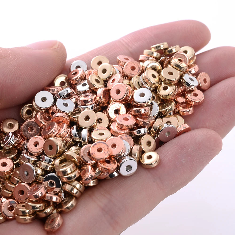A hand holds a mix of colorful geometric acrylic beads in rose gold, gold, and silver tones for jewelry making.
