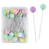 A clear box of nickel-plated dressmaking pins with colorful, purple and green heads.