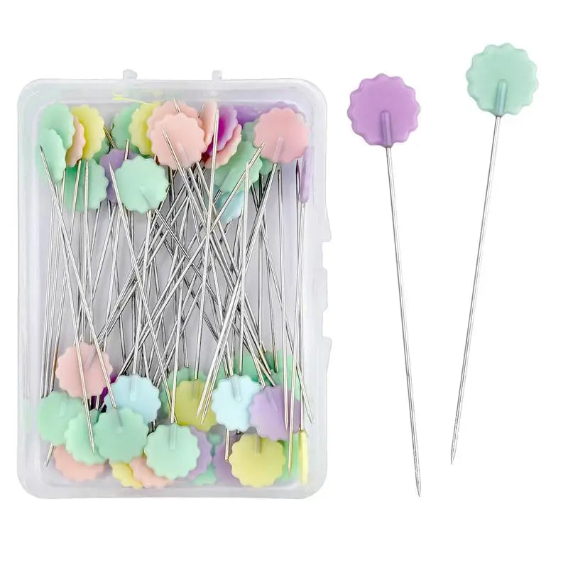 A clear box of nickel-plated dressmaking pins with colorful, purple and green heads.